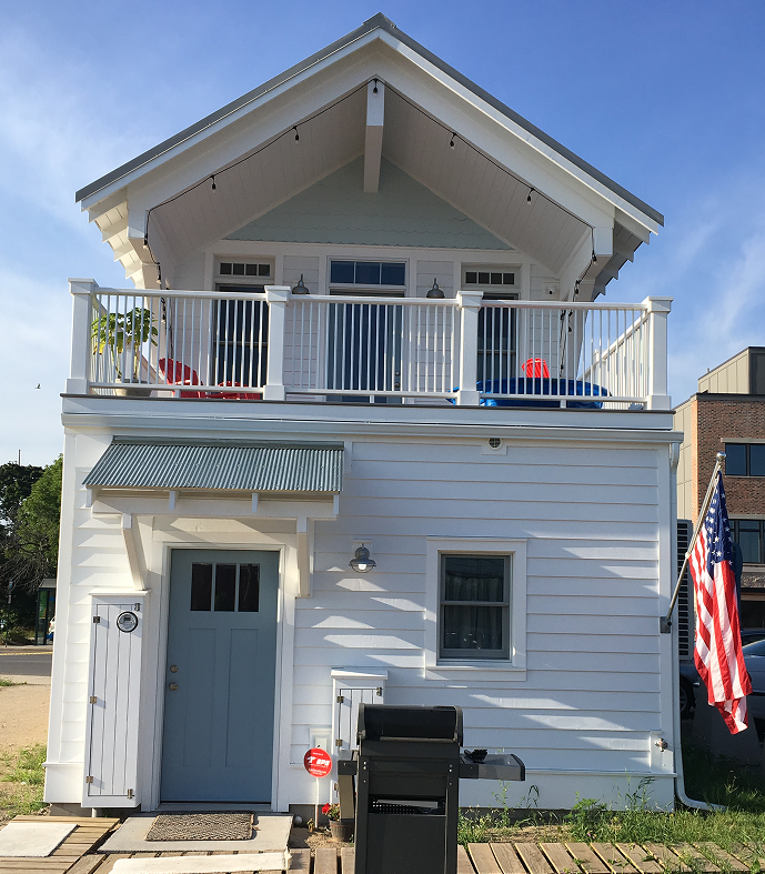 Small white two-story house with a balcony and American flag.