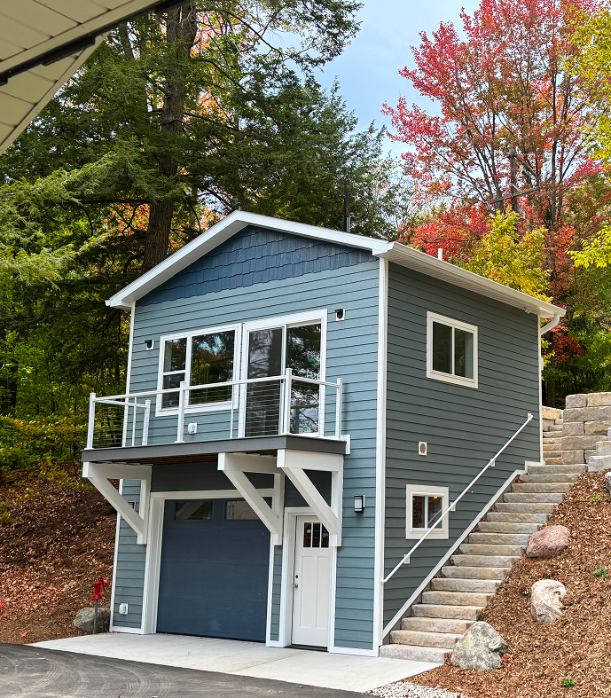 Modern blue house with a garage and balcony surrounded by autumn foliage.
