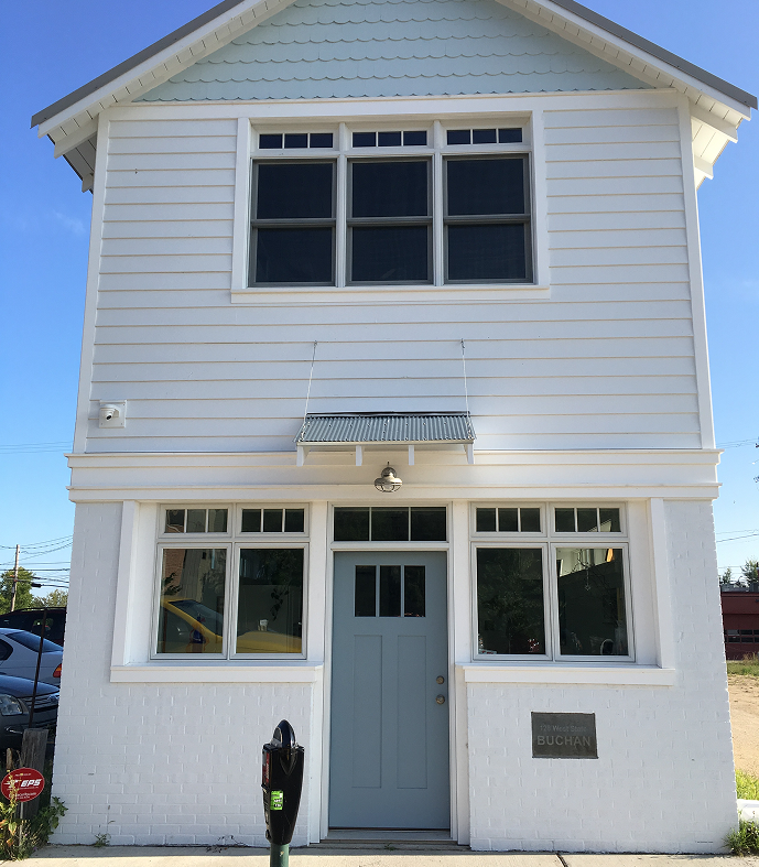 A small, white two-story house with symmetrical windows and a central door.