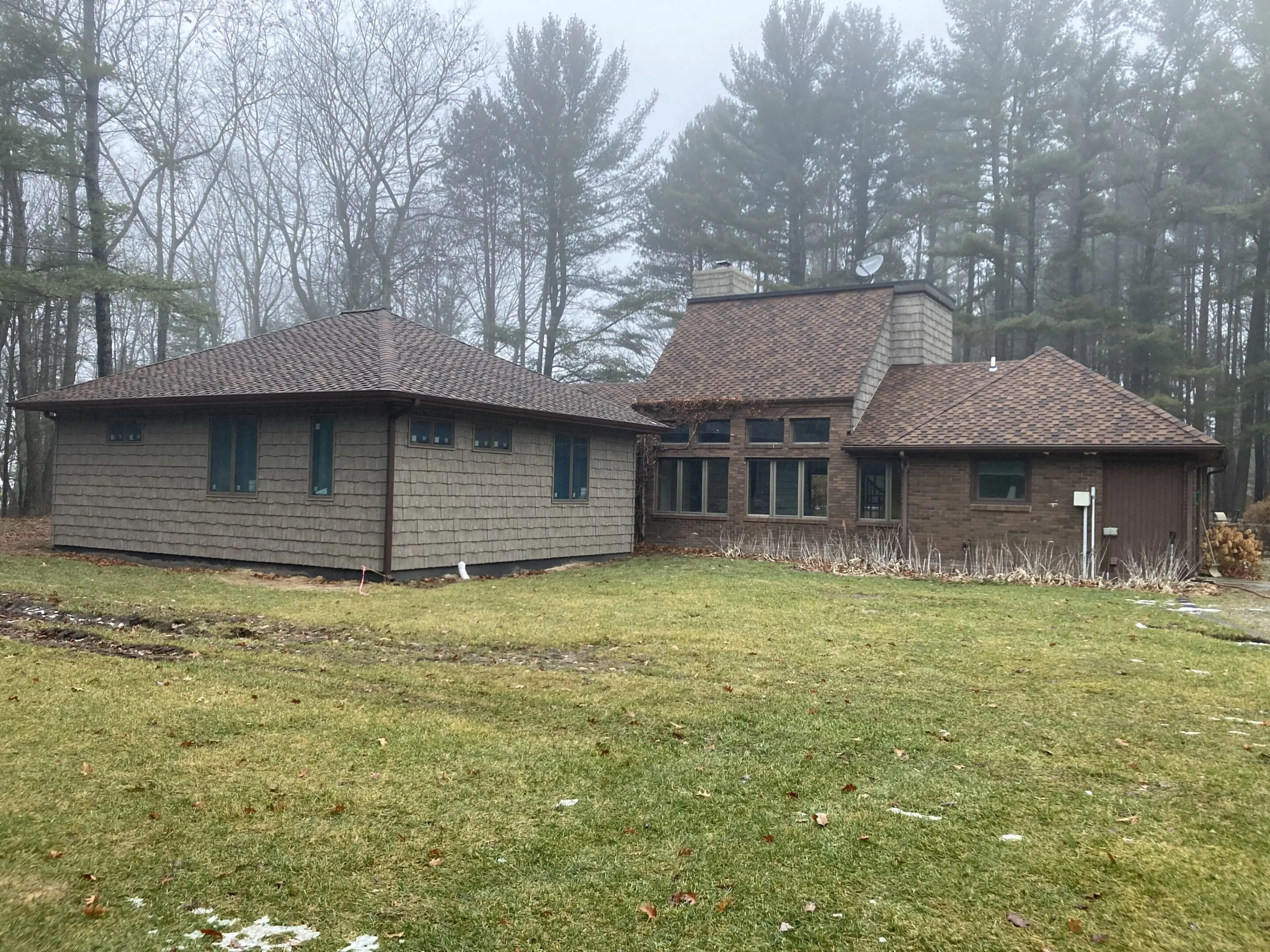 A rustic house with multiple roof levels surrounded by trees and grass.