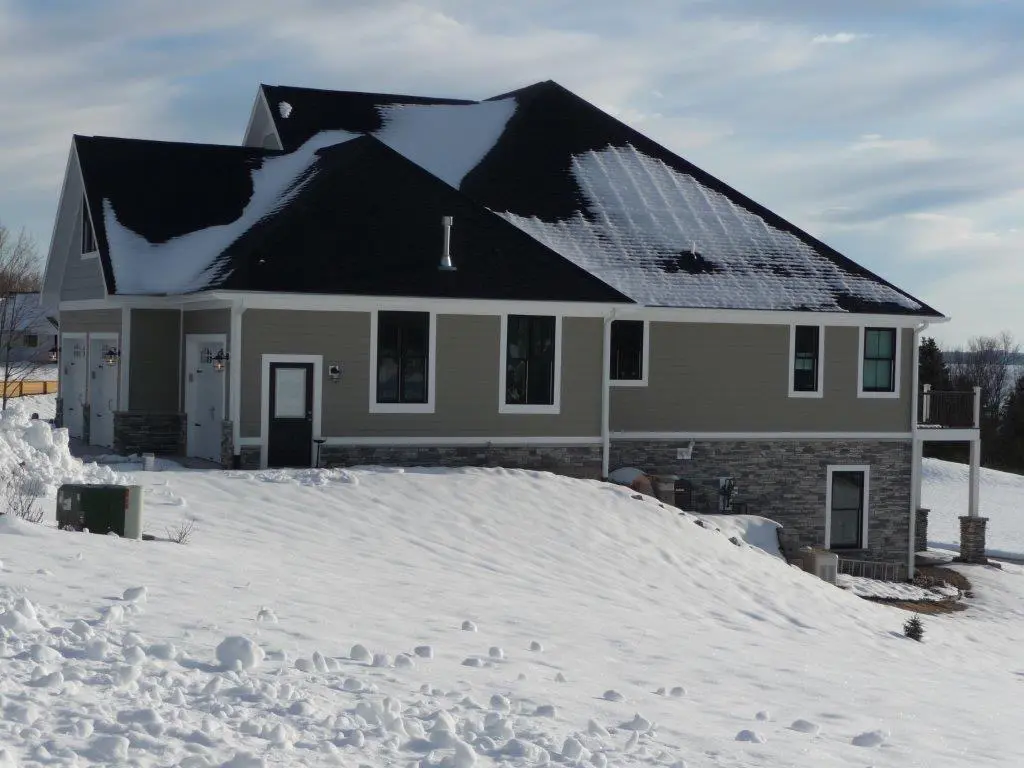 A modern house partially covered in snow under a cloudy sky.