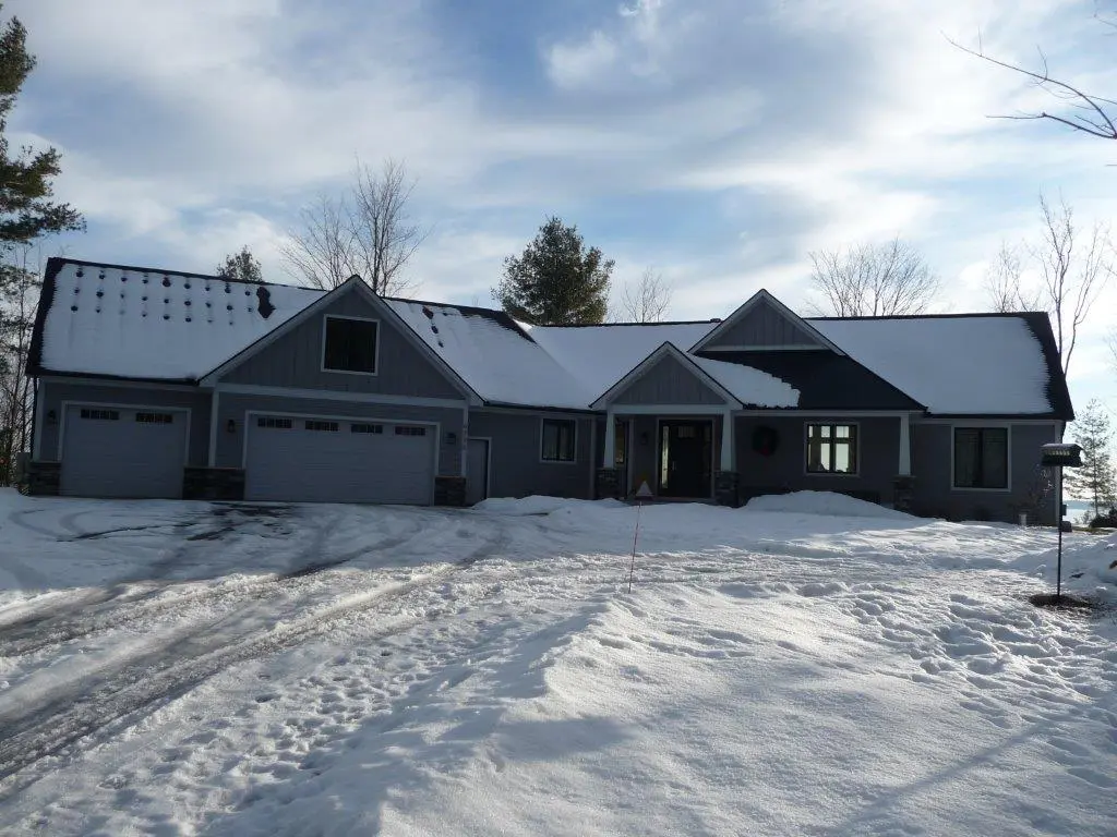 A snowy residential house with a three-car garage under a cloudy sky.